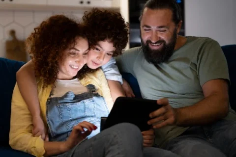 família sentada no sofá assistindo conteúdo no tablet